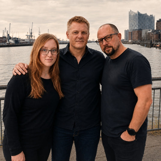 Das dreiköpfige Team des Onlineshops Dunstabzugshauben-Welt steht zusammen am Hamburger Hafen mit Blick auf die Elbphilharmonie.