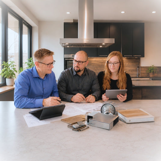 Das Team von Dunstabzugshauben-Welt bei der gemeinsamen Küchen- und Abluftplanung an einem Tisch mit Plänen, Tablets und Lüftungskomponenten in einer modernen Ausstellungsküche.
