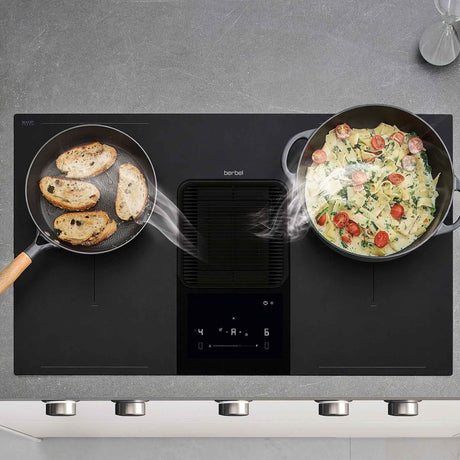 Draufsicht auf die Berbel Downline Performance mit integriertem zentralem Kochfeldabzug, Pfanne und Topf sowie sichtbar zum Abzug geführtem Kochdunst.