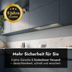 Ansicht des Falmec Lüfterbausteins Plus Green Tech, bündig integriert in dunkelblaue Küchen-Oberschränke über einer hellen Marmorarbeitsplatte. Oben links ist ein goldenes Siegel mit der Aufschrift "5 Jahre Garantie" platziert. Im unteren Bereich zeigt ein schwarzes Grafik-Overlay den Text "Mehr Sicherheit für Sie" sowie den Untertitel "5 Jahre Garantie & kostenloser Versand – deutschlandweit, schnell und versichert".