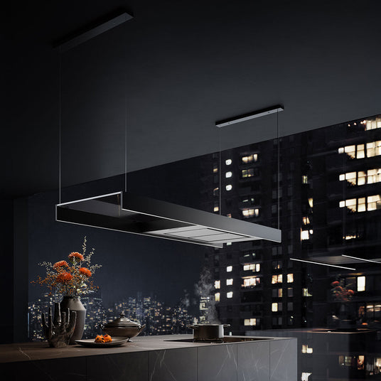 Eine schwarze Falmec Light Inselhaube hängt an filigranen Seilen über einer modernen Kücheninsel mit Kochfeld, untermalt von einem nächtlichen Skyline-Hintergrund.