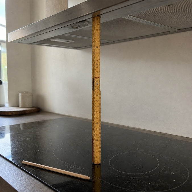 Präzise Ausmessung des vertikalen Mindestabstands zwischen Induktionskochfeld und Dunstabzugshaube mittels Holz-Zollstock.